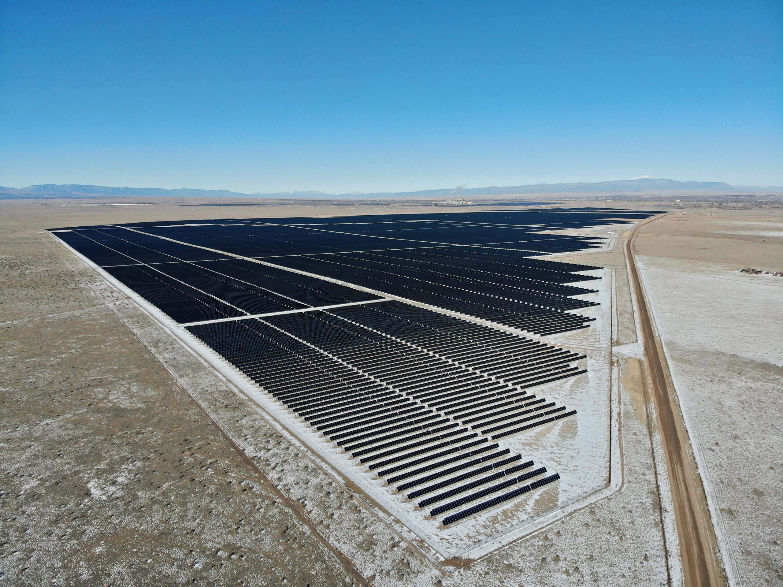 A long array of solar panels next to a dirt road that disappears into the distance